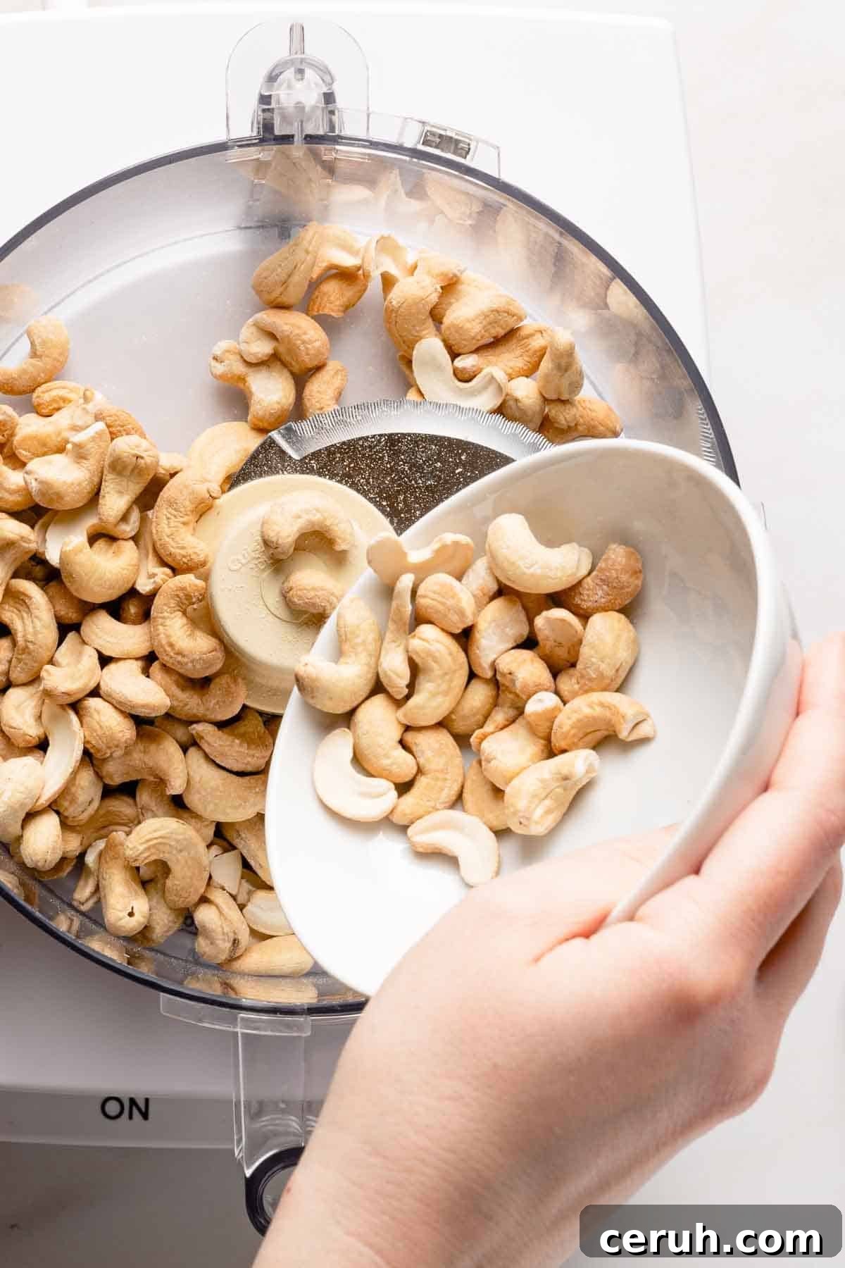 cashews being poured into bowl of food processor.