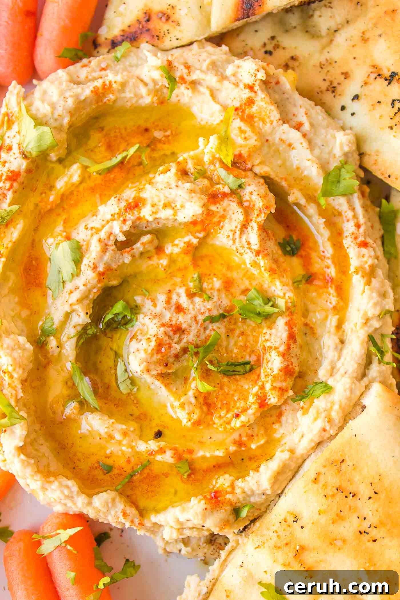Creamy hummus drizzled with olive oil surrounded by wedges of pita and baby carrot.
