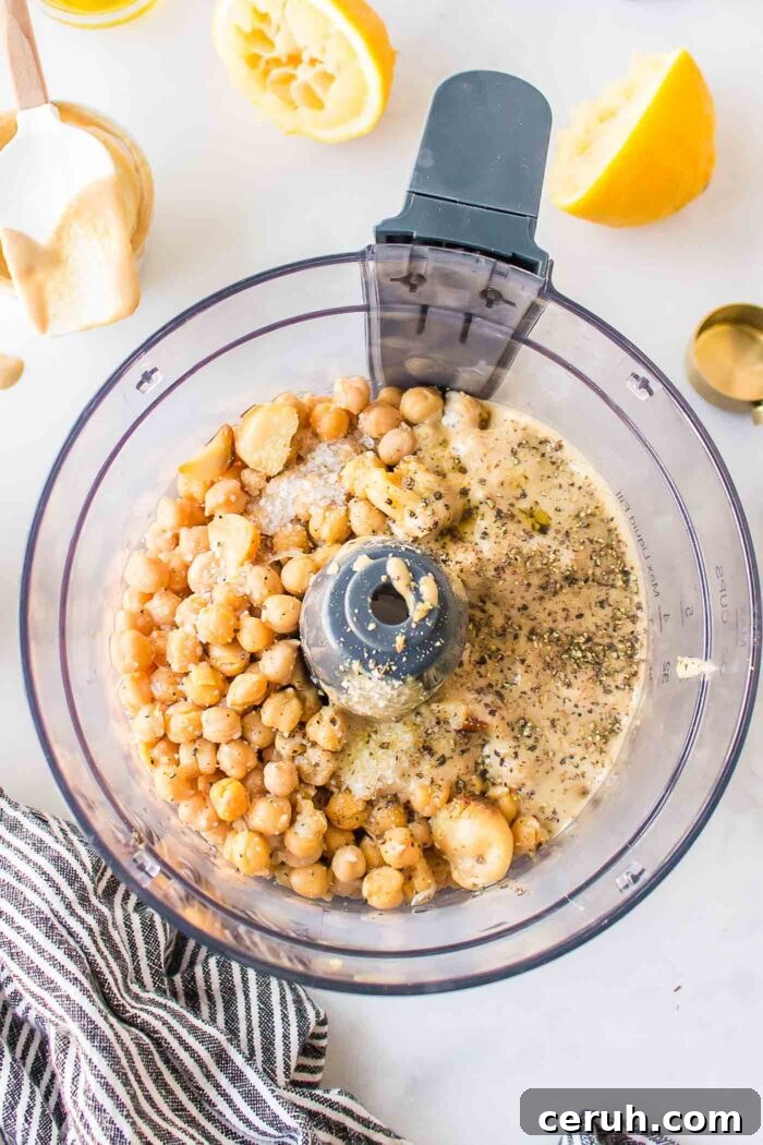 Chickpeas, tahini and cloves of roasted garlic in a food processor container.