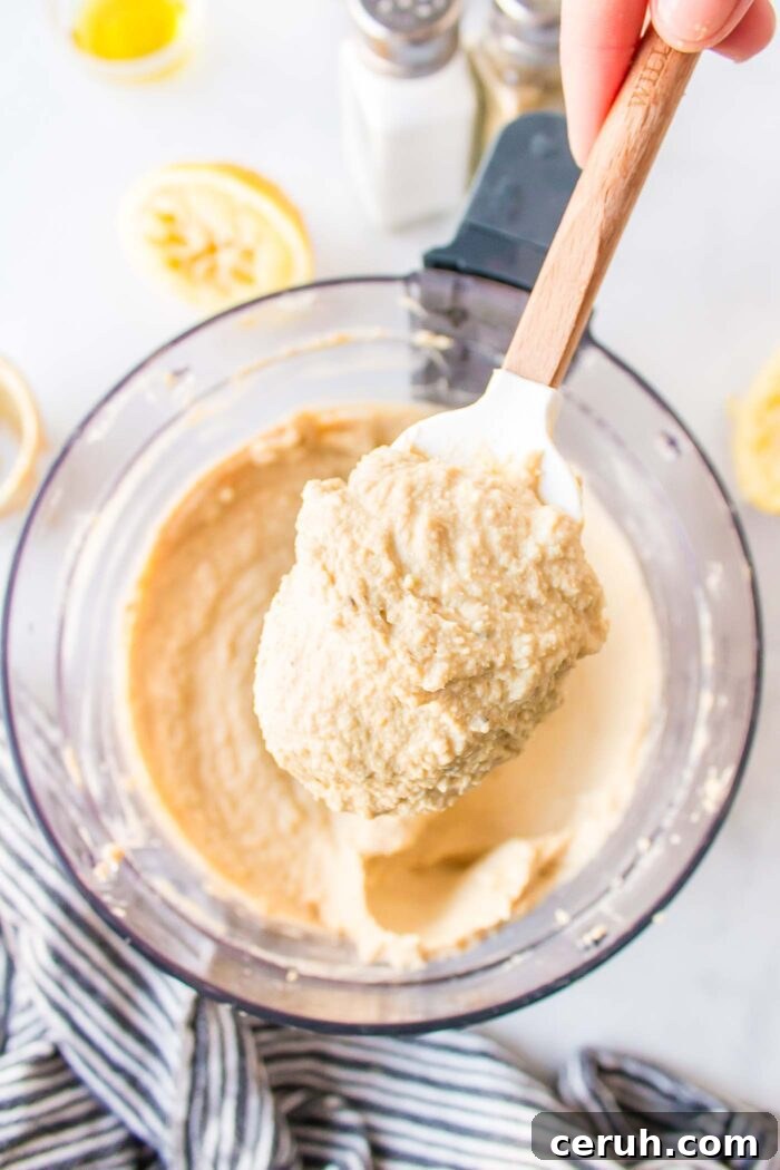 A hand holding a spatula with a large scoop of hummus on it.