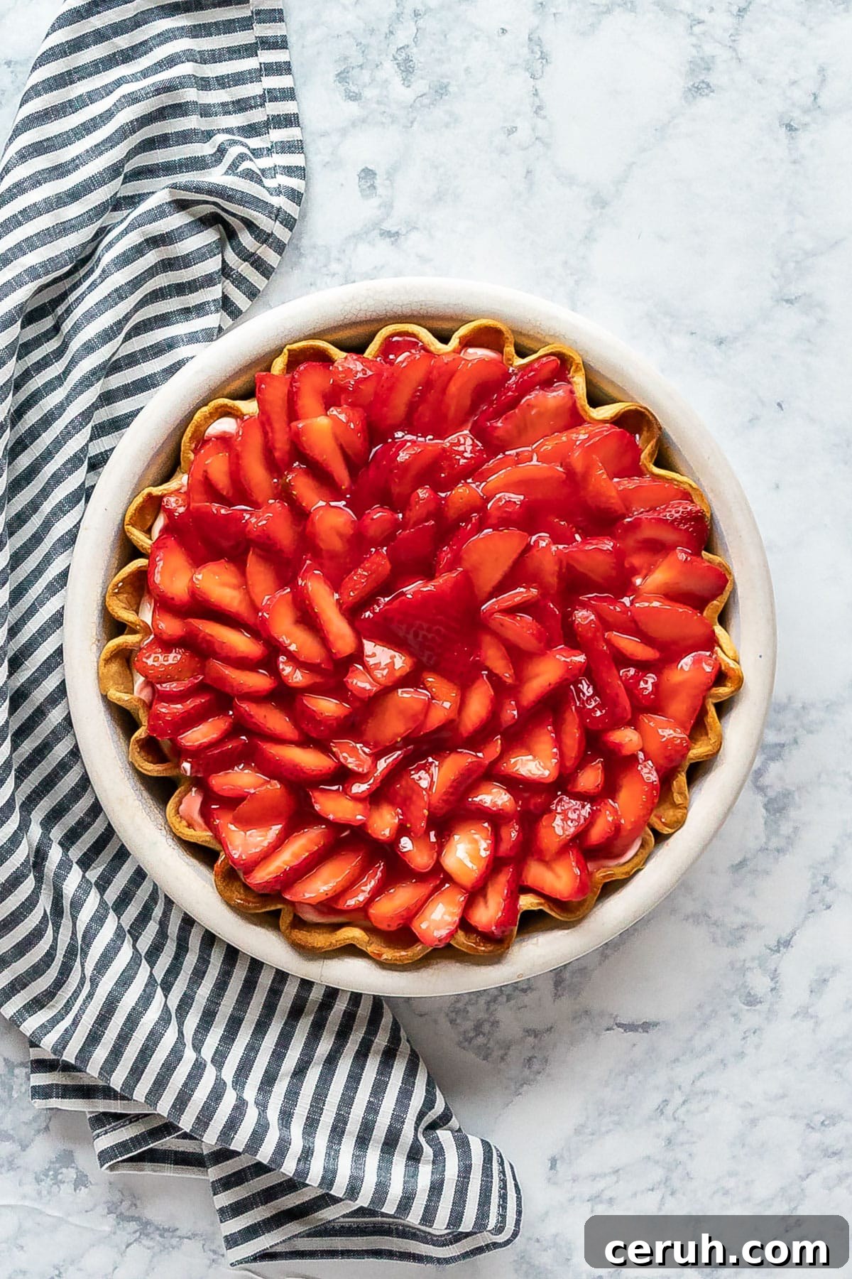 An overhead image of a strawberry cream pie with a striped napkin next to it.