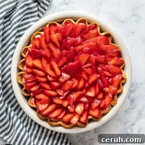 An overhead image of a strawberry cream pie with a striped napkin next to it.