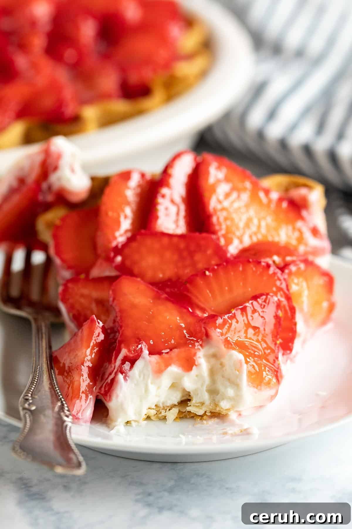 An image looking straight at a slice of strawberry cream cheese pie with a bite taken off revealing the creamy filling with the strawberries on top.