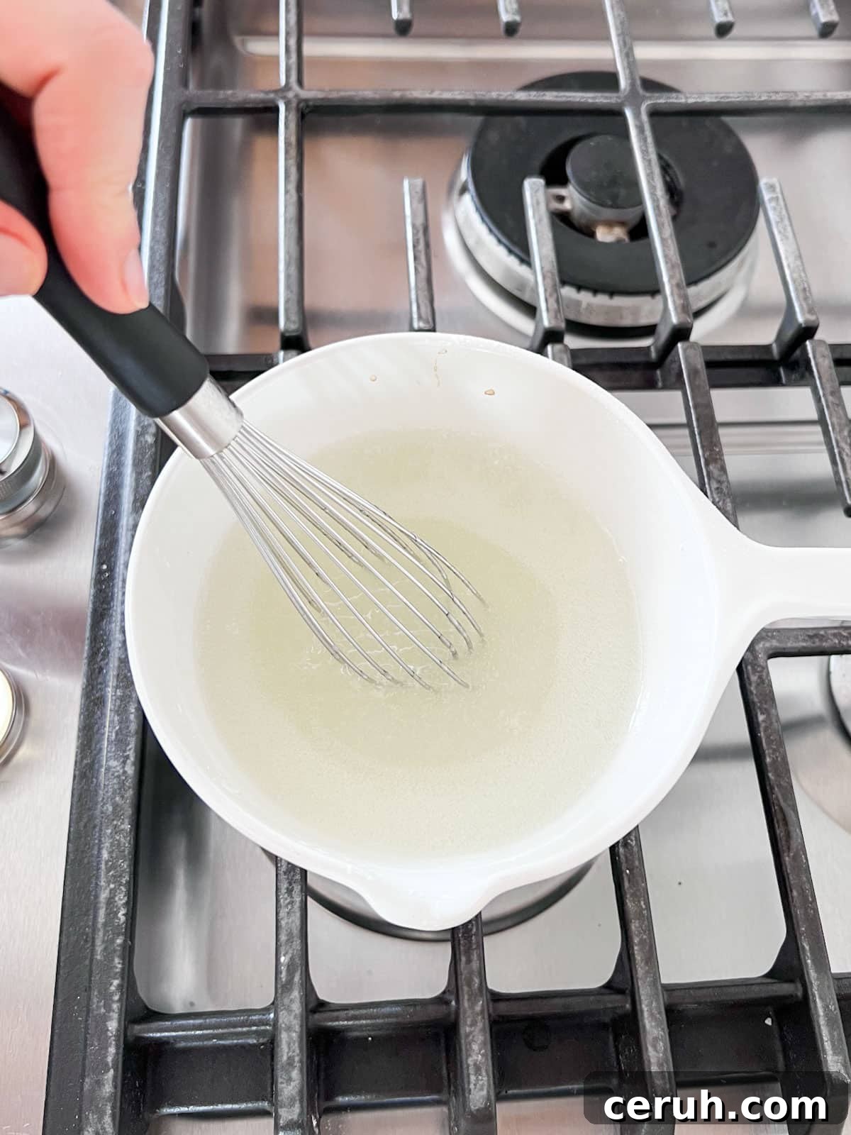 Glaze mixture thickening on the stove with a whisk in it.
