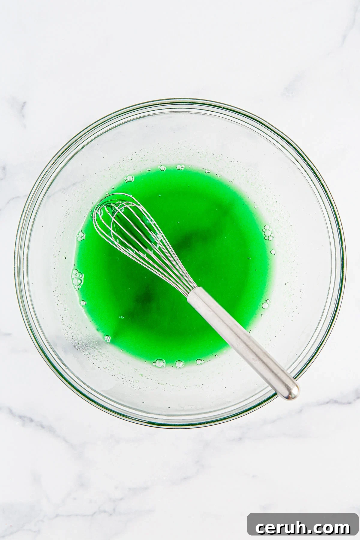Lime gelatin mixed with water in a glass mixing bowl.
