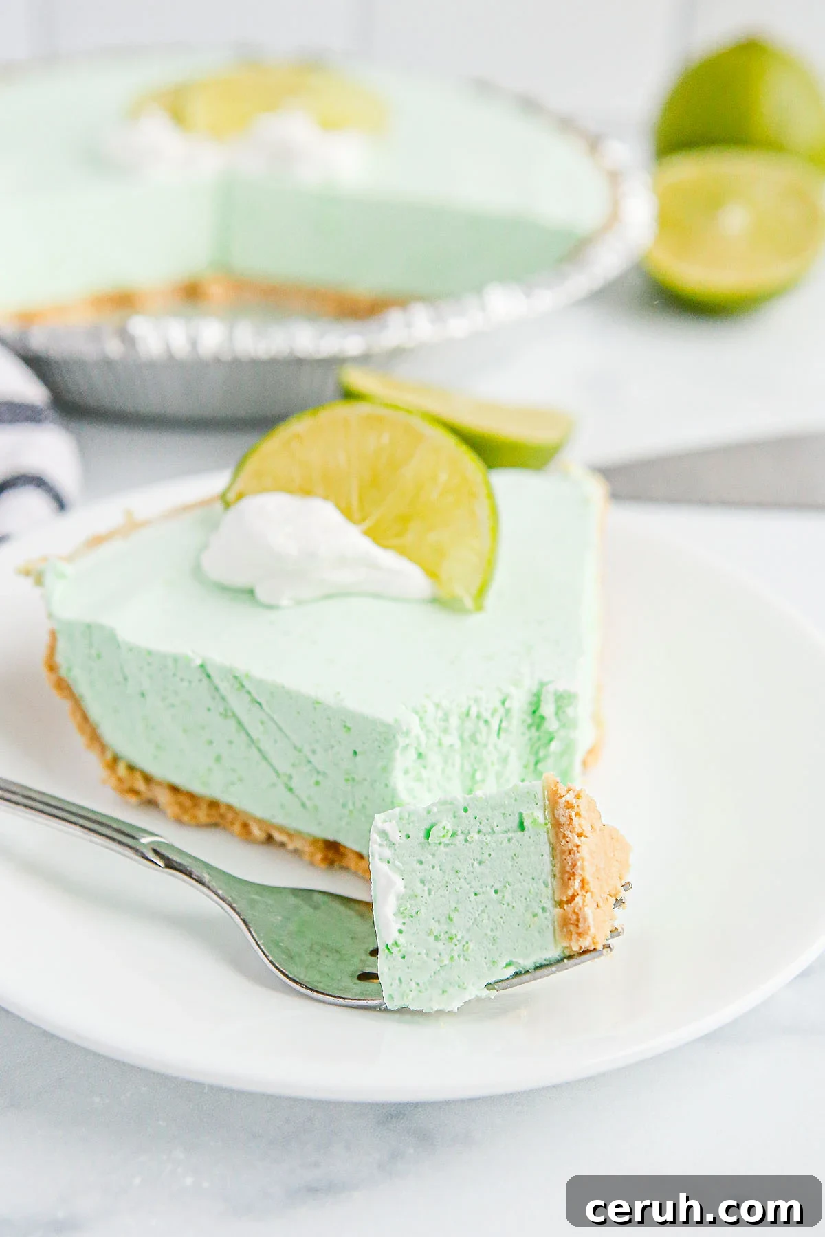 Slice of Lime Pie on a white plate with a bite on a fork.