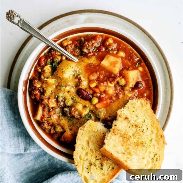 A bowl of shepherd's pie chili topped with herbs, served with a spoon and two slices of toasted bread on the side.