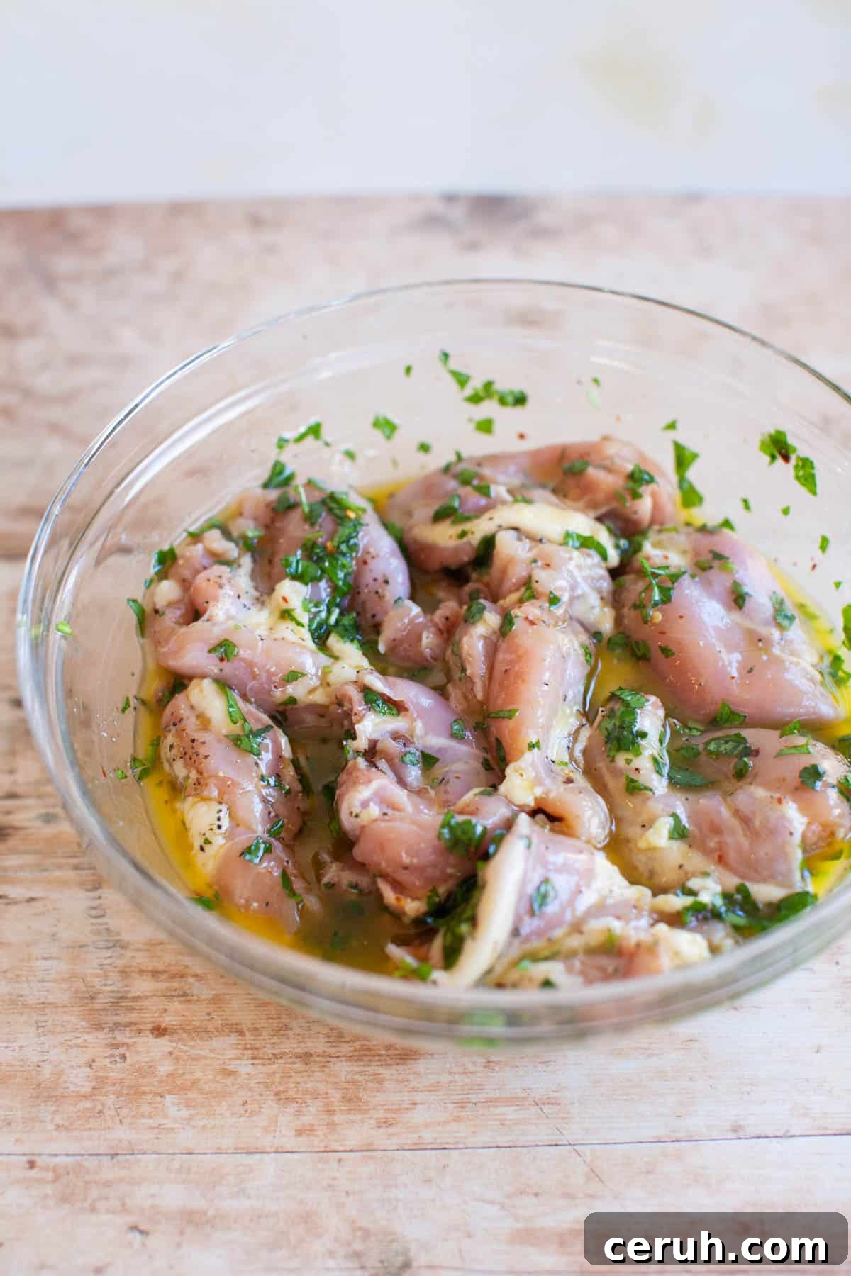 raw chicken thighs resting in lemon marinade in a glass bowl.