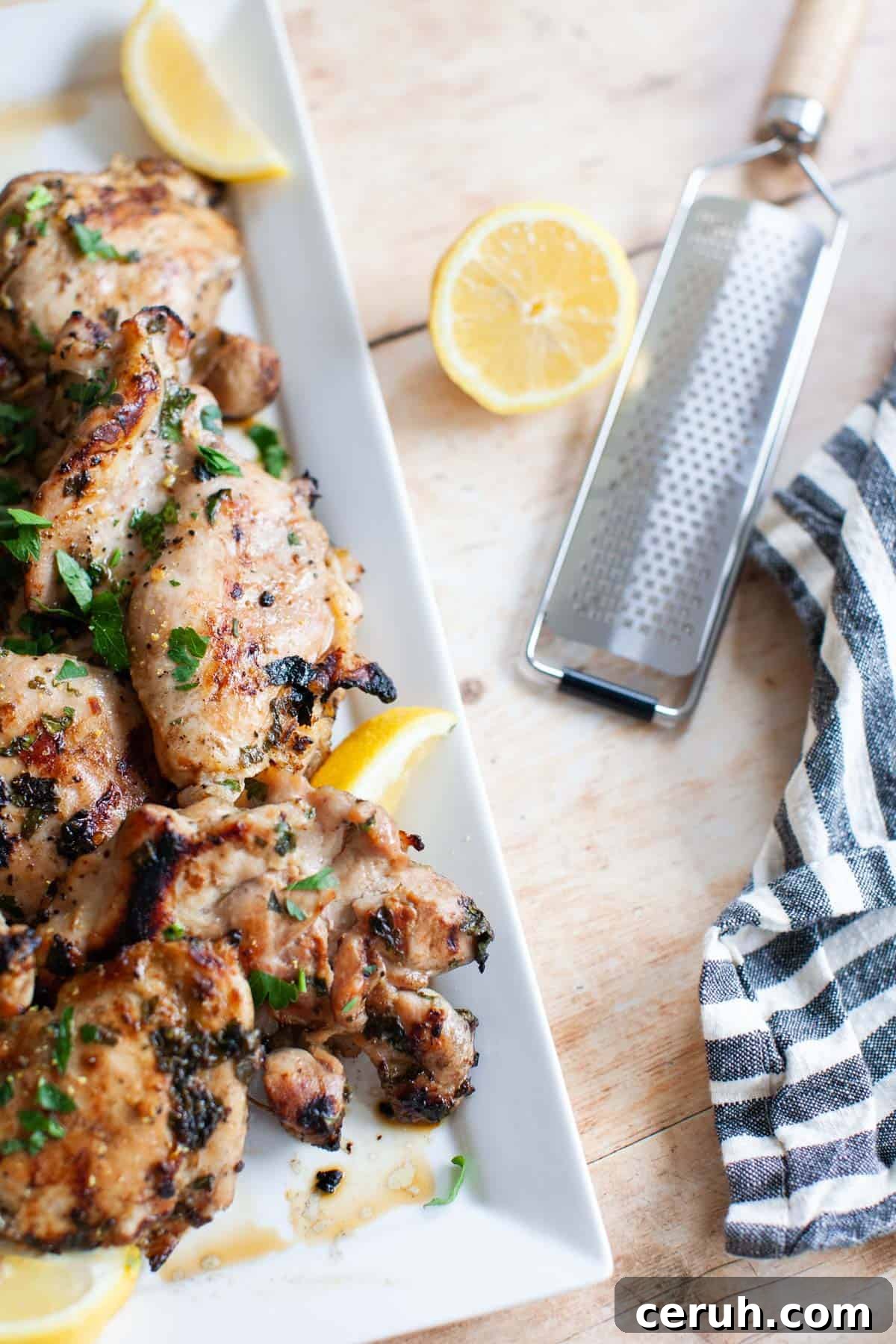 a lemon zester on a table with a half a lemon and lemon chicken and a tea towel.