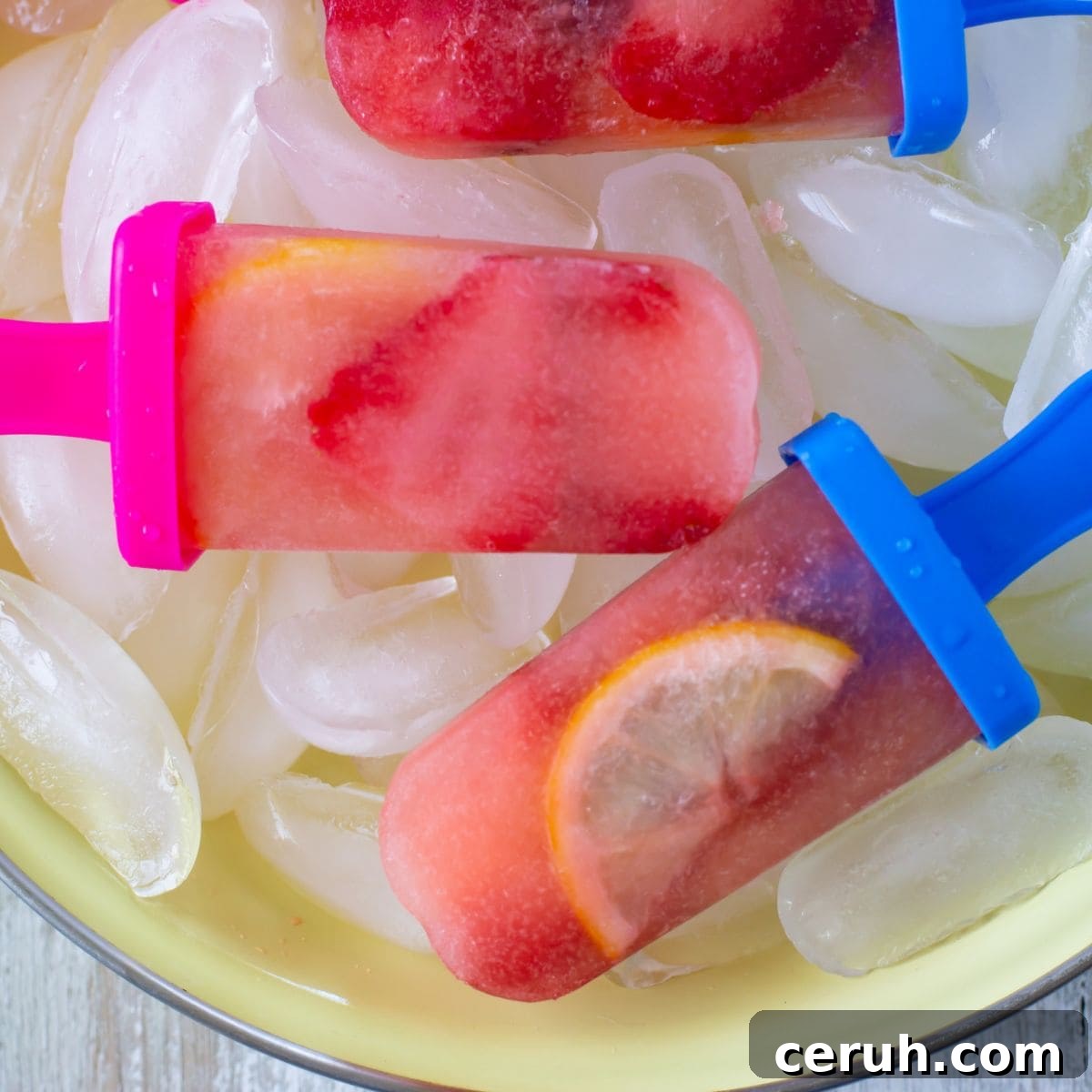 Three strawberry lemonade ice pops in a pie plate on ice cubes.