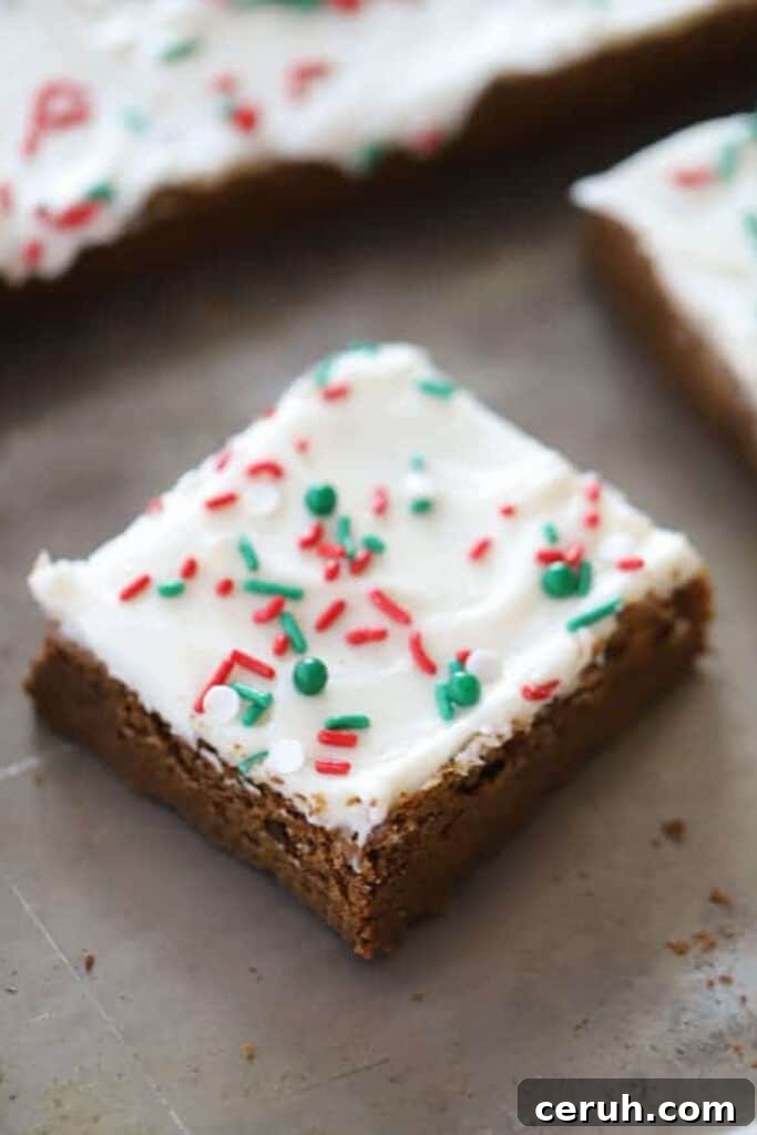 A baking sheet with gingerbread cookie bars topped with cream cheese frosting and red and green sprinkles.