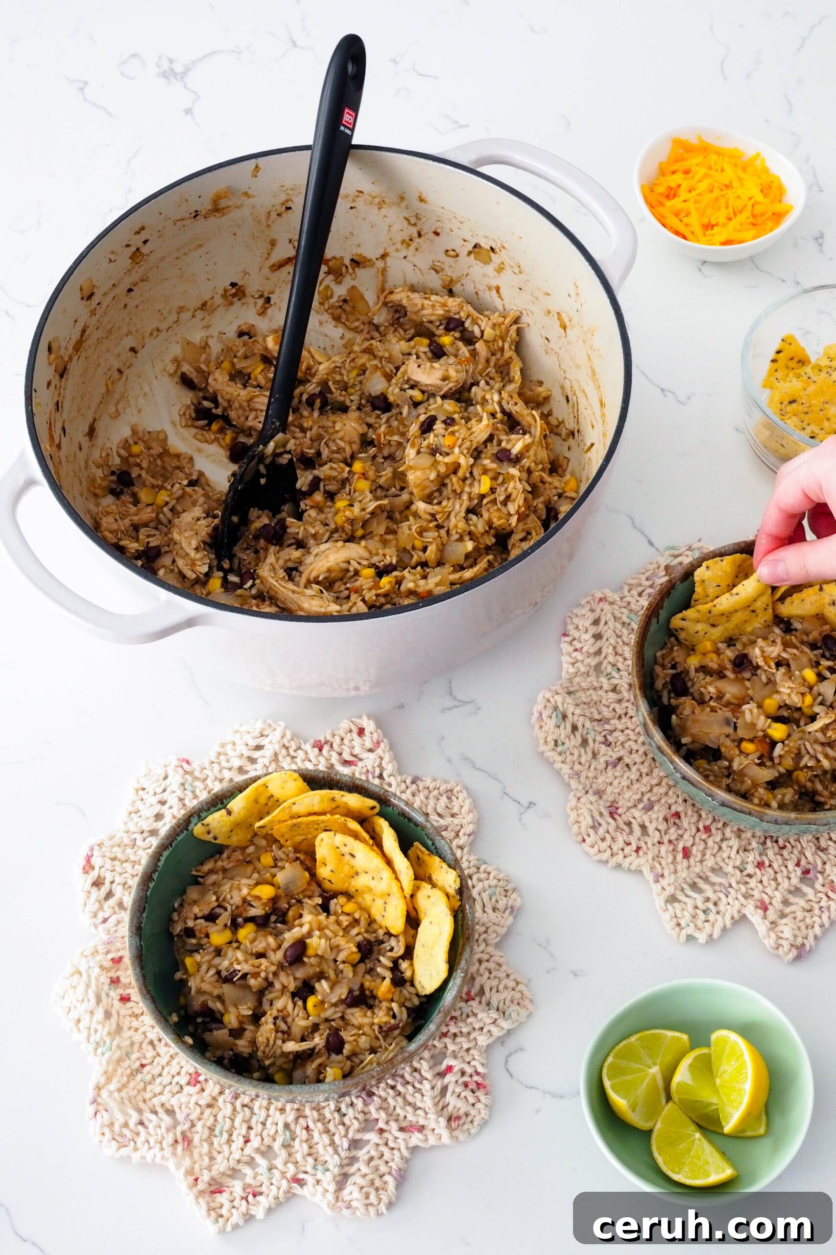 A hand adds tortilla chips to a bowl of one-pot chicken and brown rice.