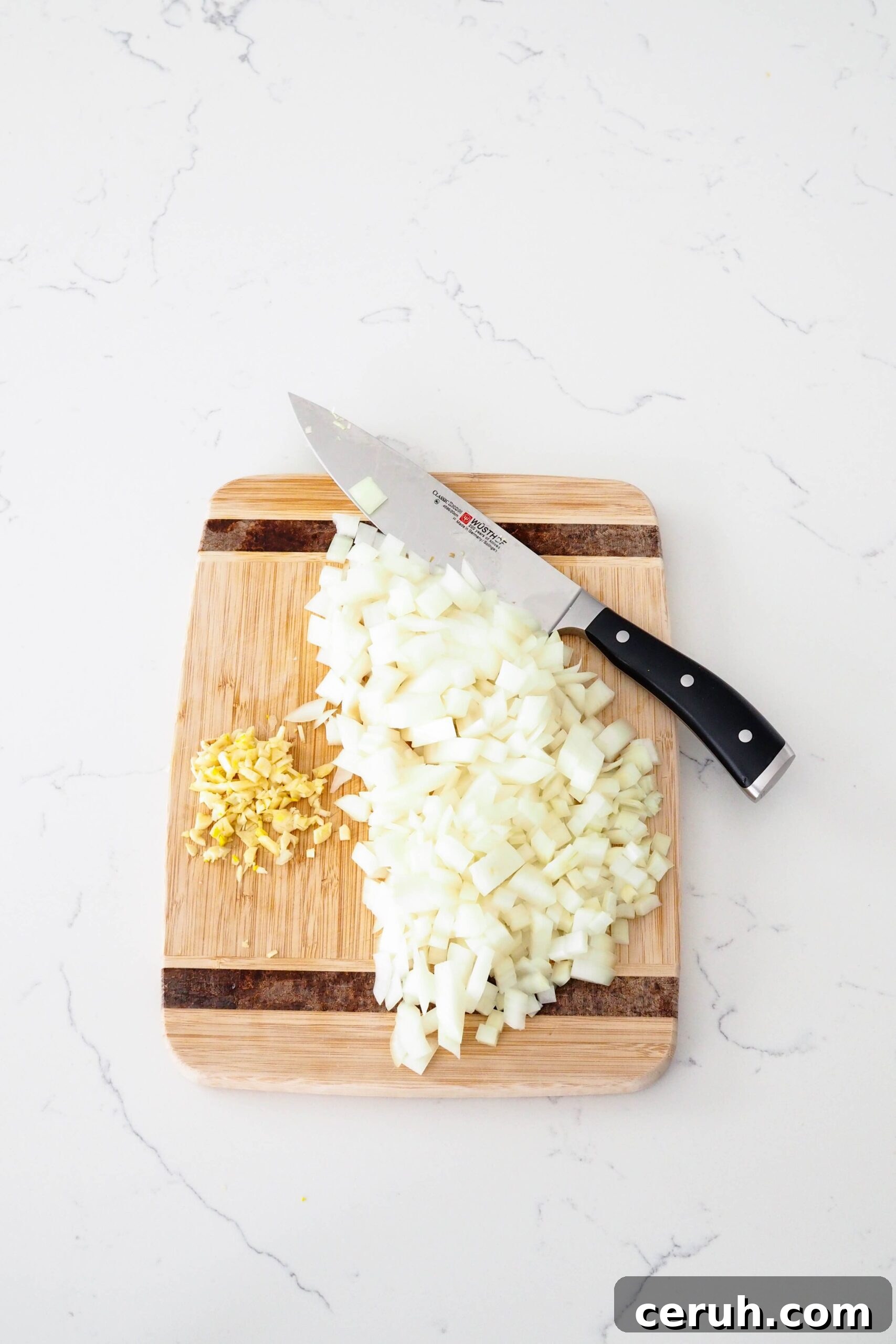 Diced onion and minced garlic on a cutting board with a knife.