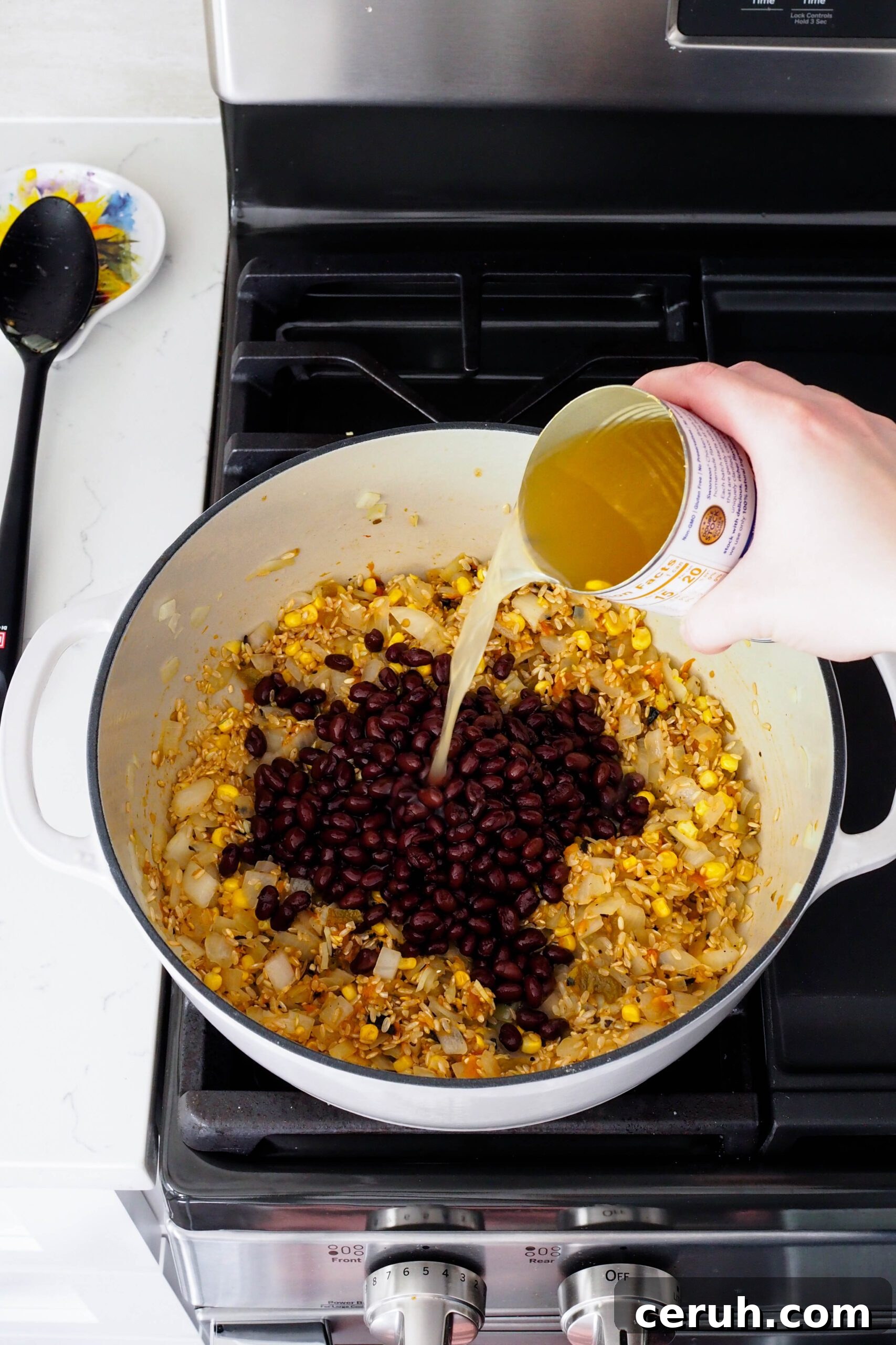 Chicken broth is poured into a Dutch oven filled with rice, corn, and beans.