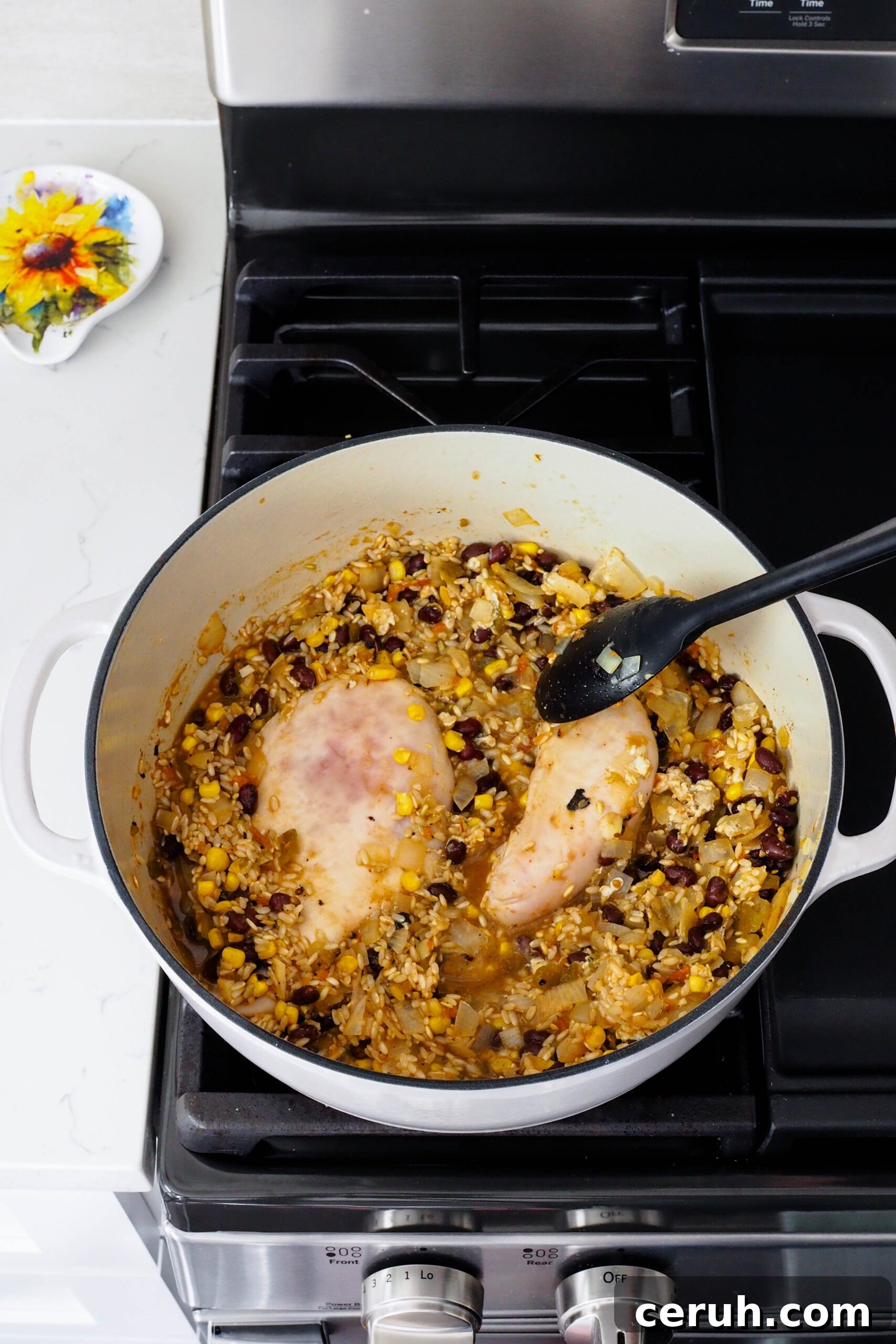 A spoon separates two chicken breasts in a pot, both still pink.