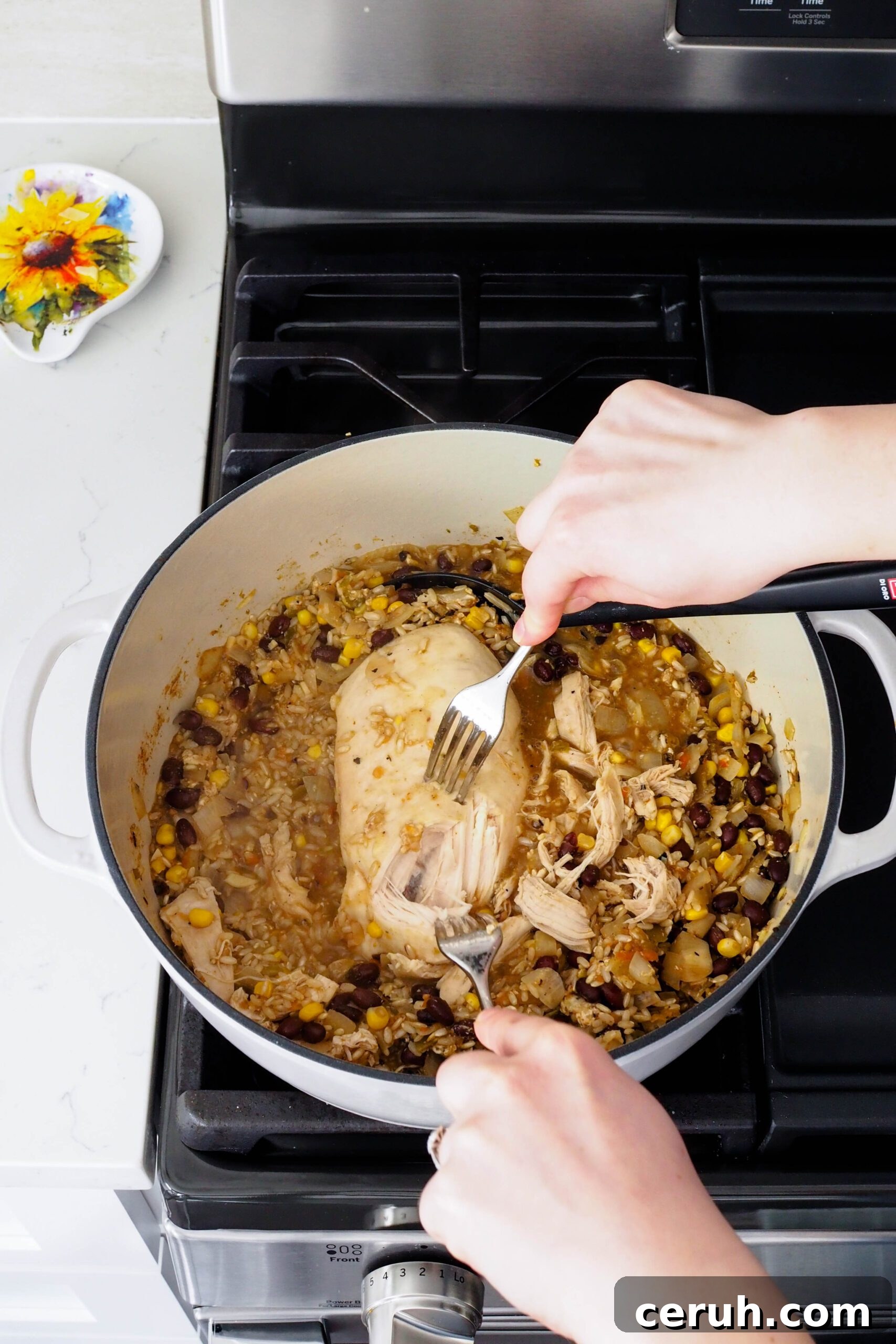 Two hands use forks to shred chicken in a pot.