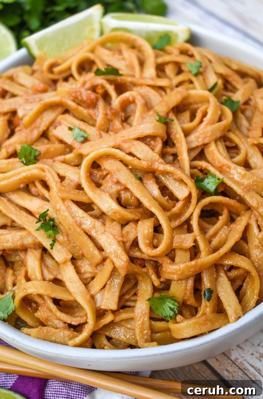 chinese peanut butter noodles in a white serving bowl with a pair of chop sticks on the side