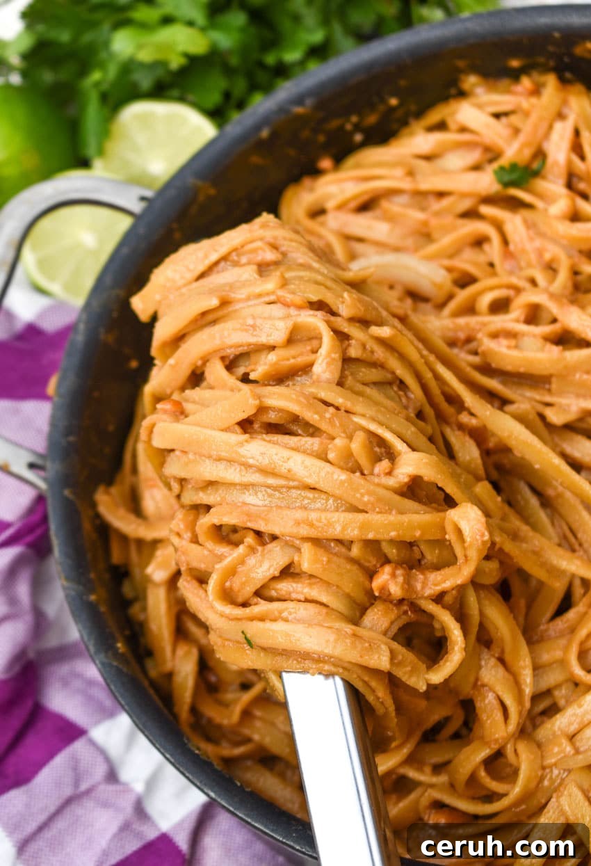 a silver ladle scooping peanut butter noodles out of a large black skillet