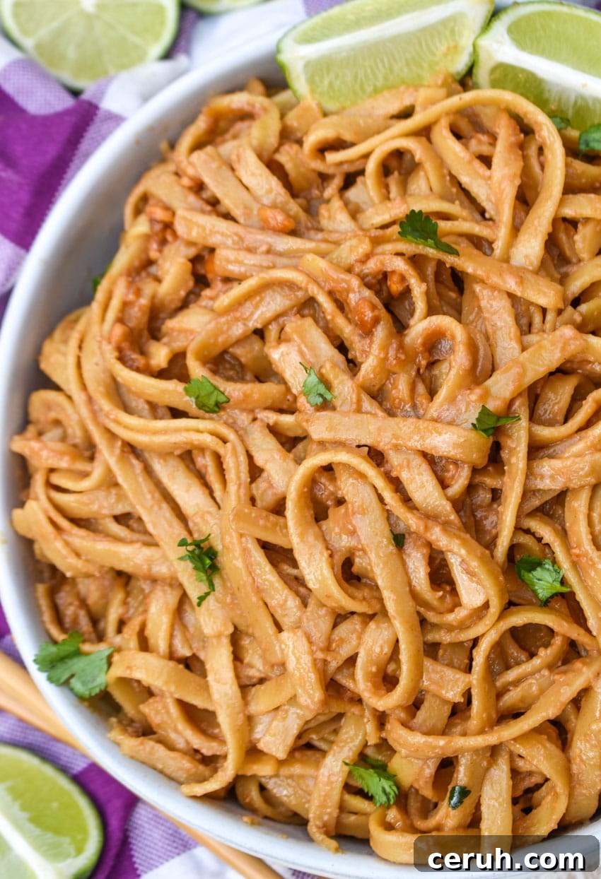 chinese peanut butter noodles in a white serving bowl with a pair of chop sticks on the side