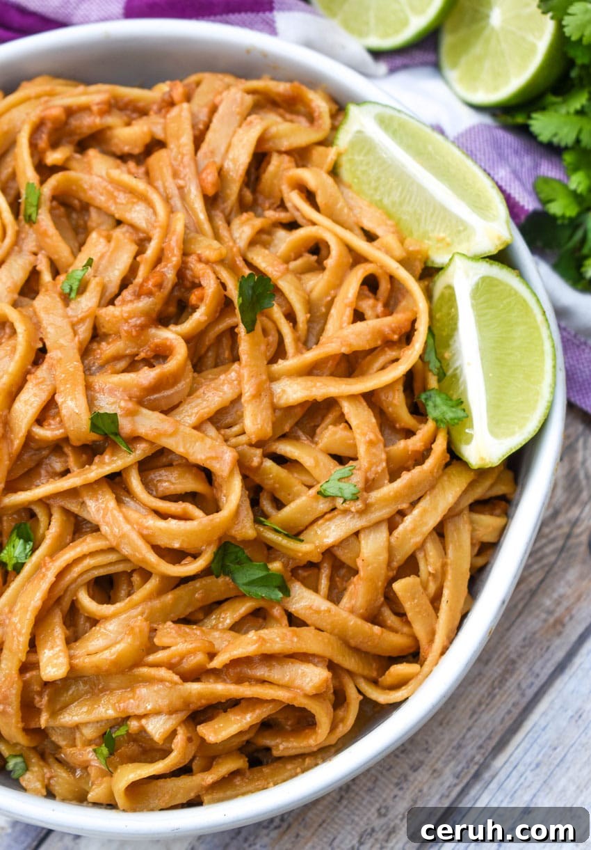 chinese peanut butter noodles in a white serving bowl with a pair of chop sticks on the side