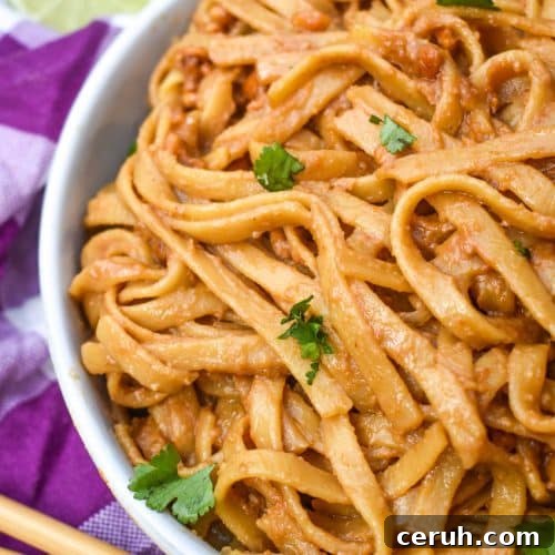 chinese peanut butter noodles in a white serving bowl with a pair of chop sticks on the side