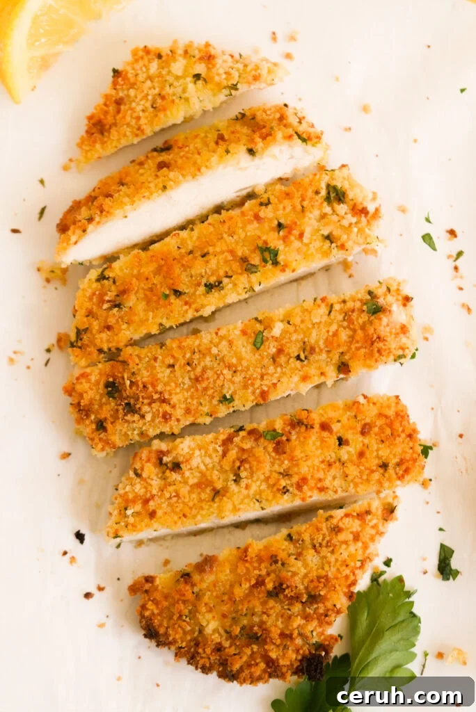 flat lay shot of a sliced baked and breaded chicken cutlet with fresh parsley and a lemon wedge.