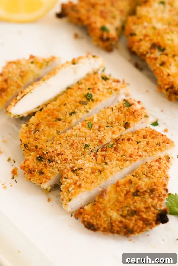 45 degree hero shot of a baked chicken cutlet sliced and garnished with fresh parsley and a lemon wedge.