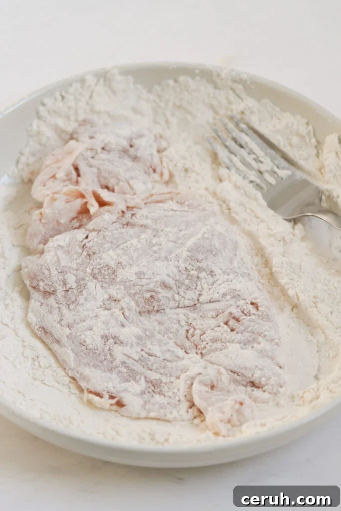 process shot - pounded chicken breast cutlet being tossed in flour dredge.