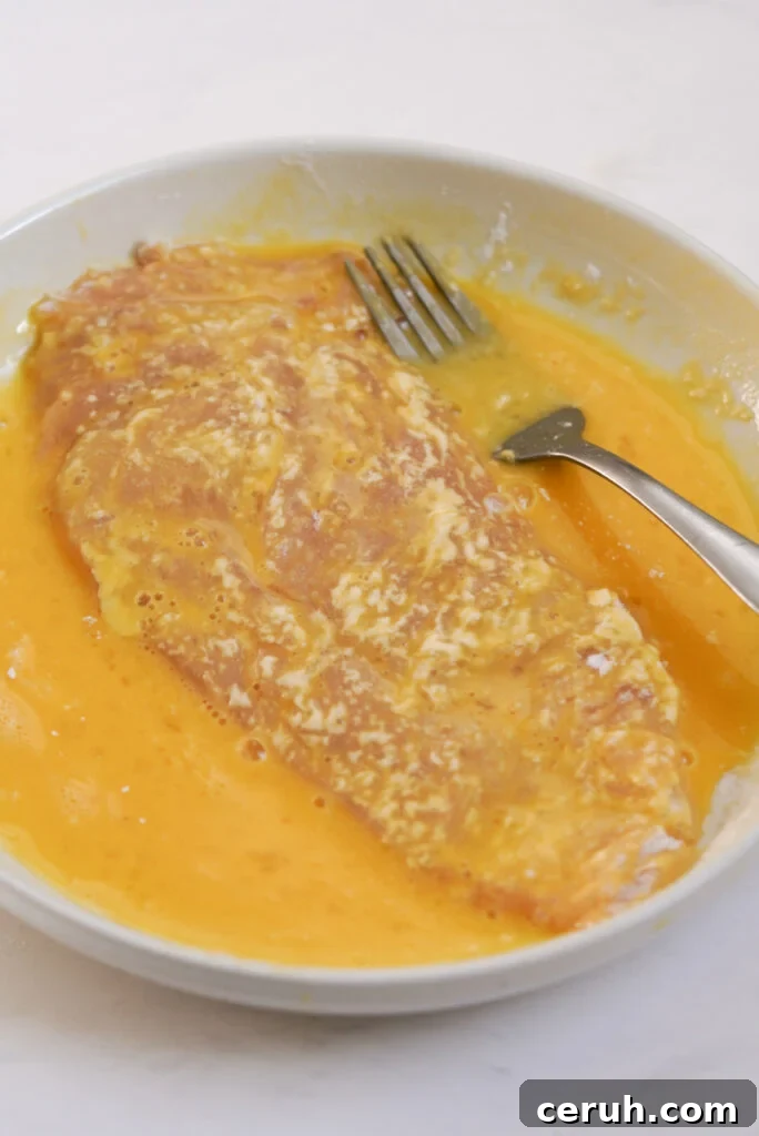 process shot - dredged chicken cutlet being coated in egg wash.