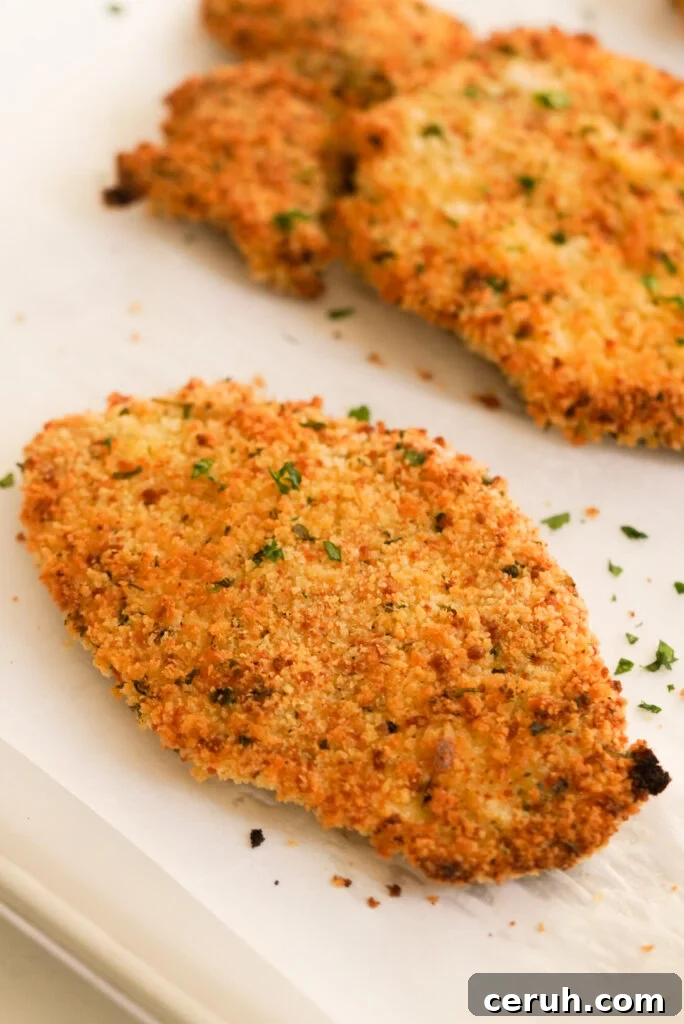 closeup shot of a baked chicken cutlet on a parchment lined sheet pan.