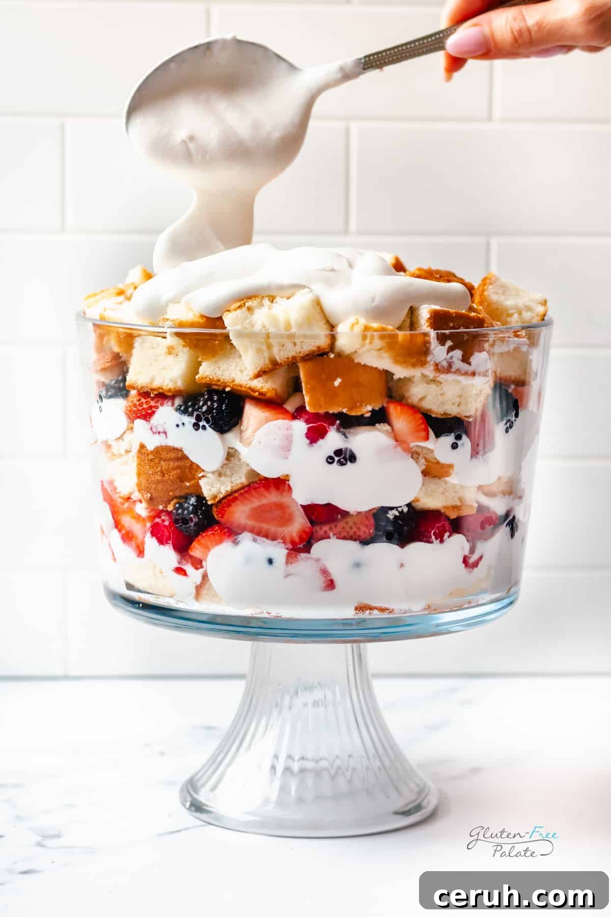 Gluten-Free Berry Trifle with Cake Layers and Whipped Cream 6 whip cream being spooned onto a gluten free trifle