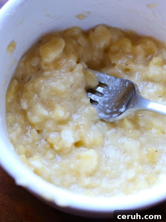 This easy banana cookies recipe makes soft, sweet cookies loaded with banana flavor, topped with caramel frosting. Mix the dough in one bowl! Close up of mashed bananas in a bowl with a fork.