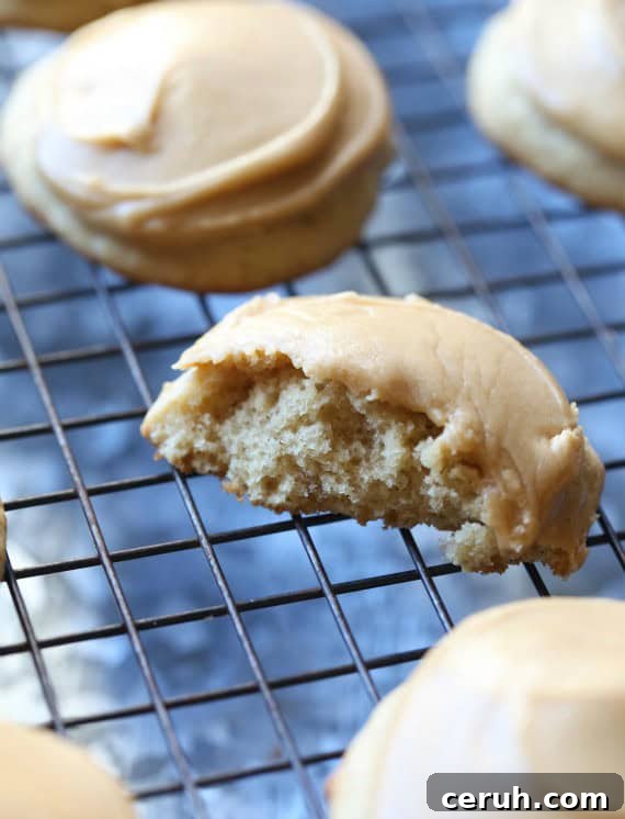 Frosted banana cookies with a bite taken. Frosted banana cookies on a wire rack with a bite missing from one cookie.