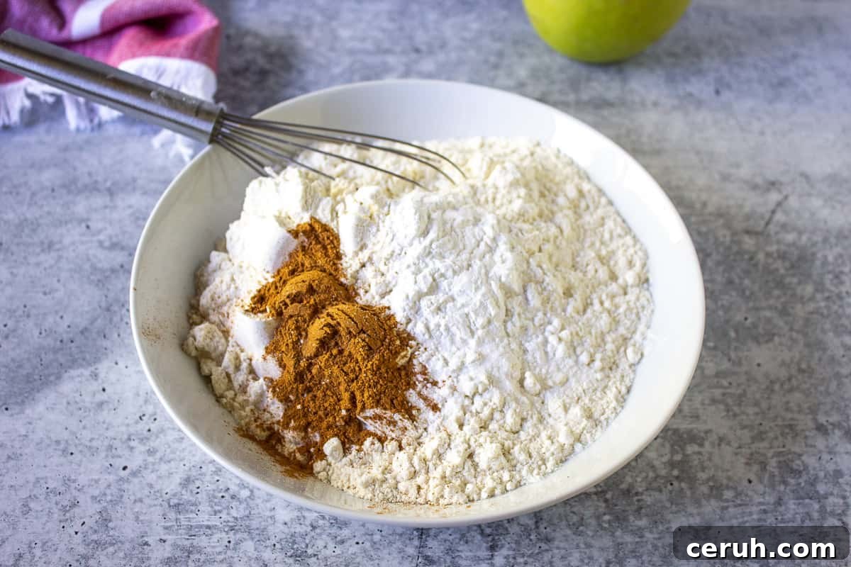 Flour and cinnamon in a white bowl with a small wire whisk.