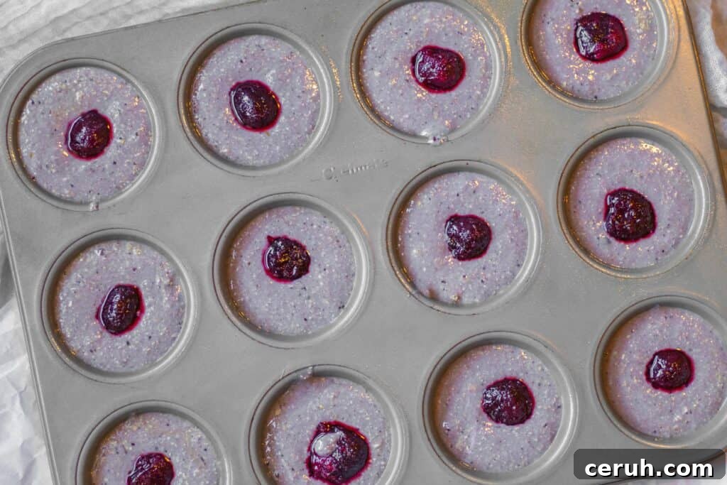 muffin batter in muffin tins with cherry pushed into the middle of each muffin