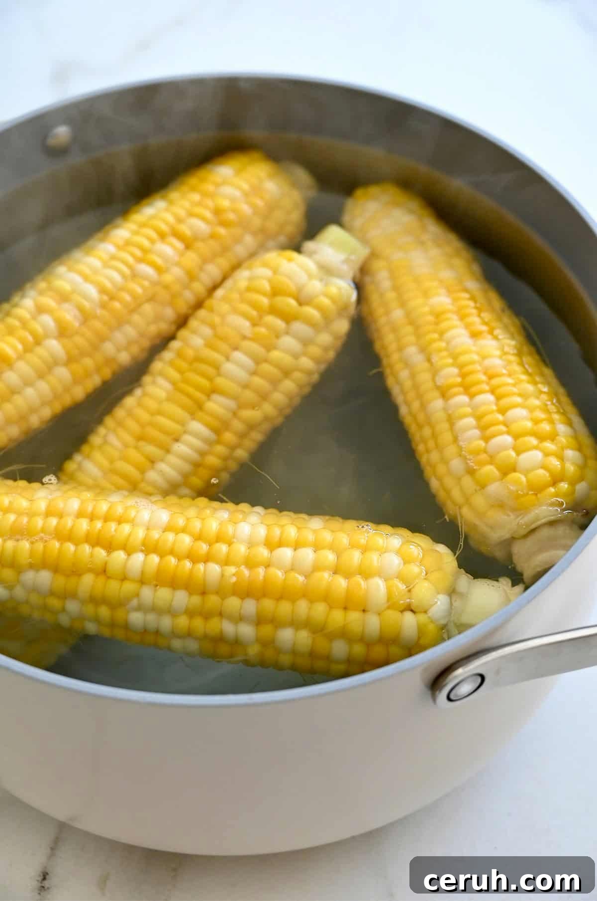 Four ears of corn are boiling in a large pot of water.
