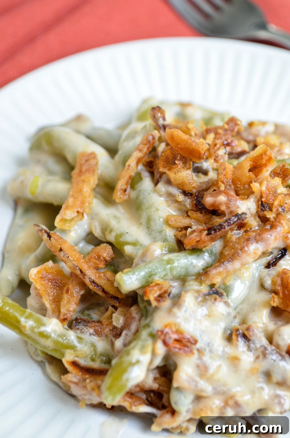 Creamy Slow Cooker Green Bean Casserole for Holidays 8 A serving of green bean casserole on a white plate, topped with french fried onions.