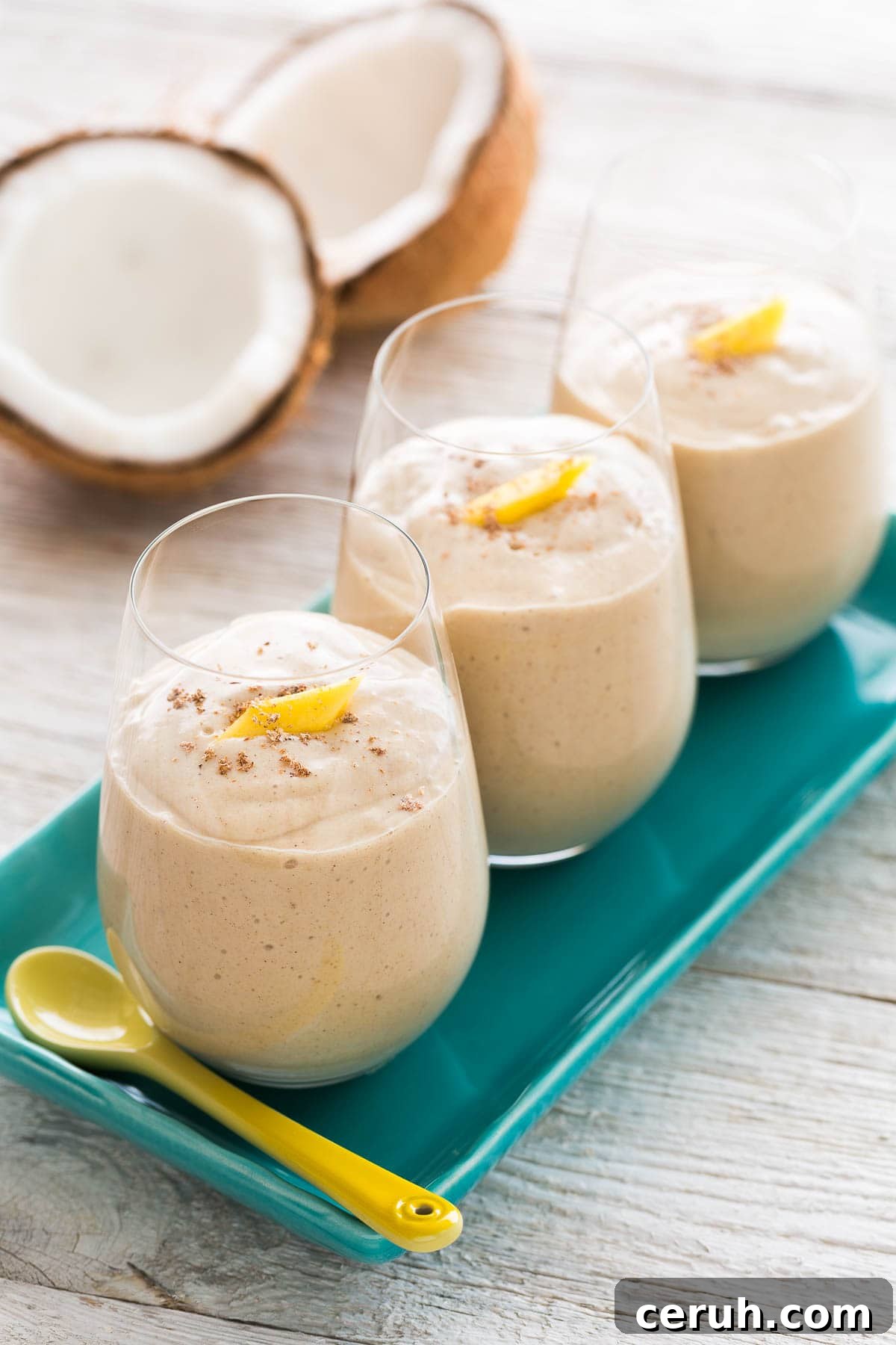 Creamy coconut mango smoothie in 3 glasses on a blue plate.