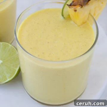 A bright yellow mango pineapple smoothie in a glass with lime and fruit wedge.