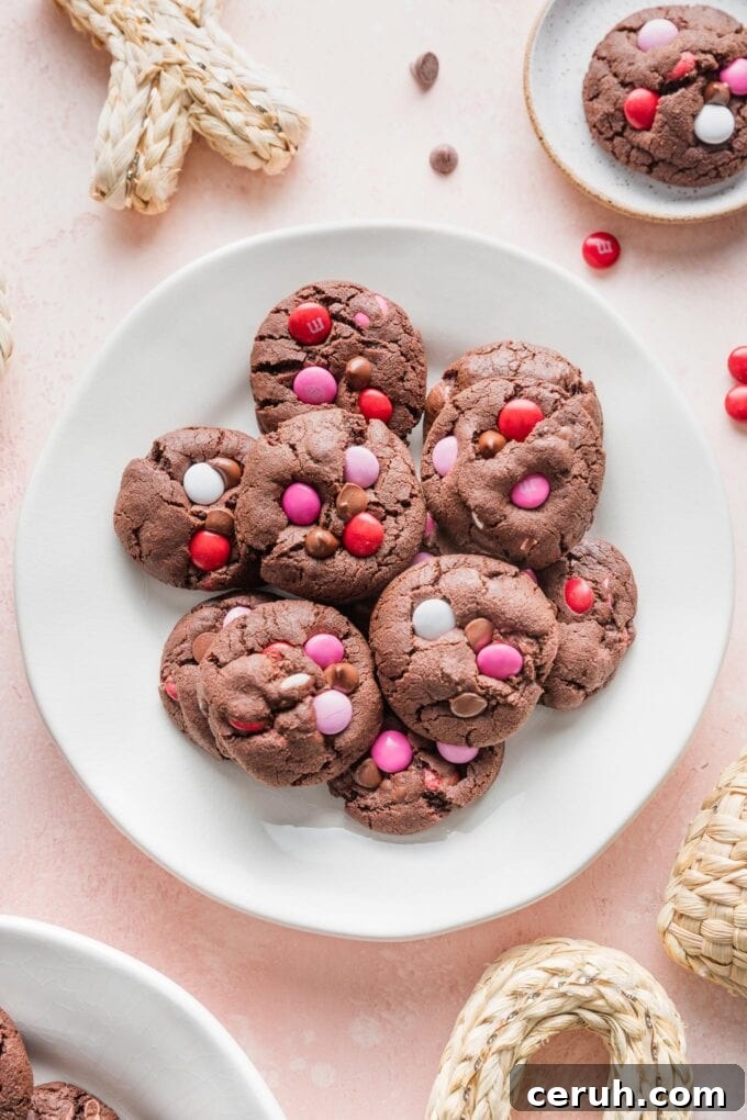 Small white plate on a pink counter, filled with double chocolate cookies with Valentines M&Ms and chocolate chips.