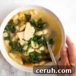 a hand holding a bowl of Tuscan bean soup with a spoon in it.