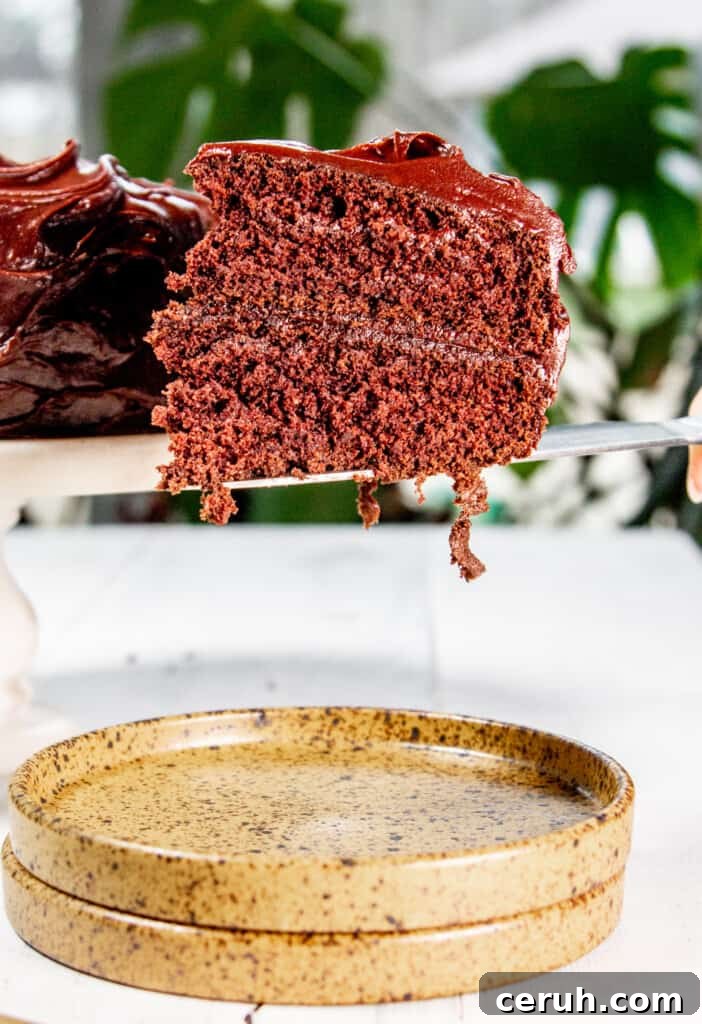 A knife holding a slice of chocolate devils food cake hovering over a yellow plate