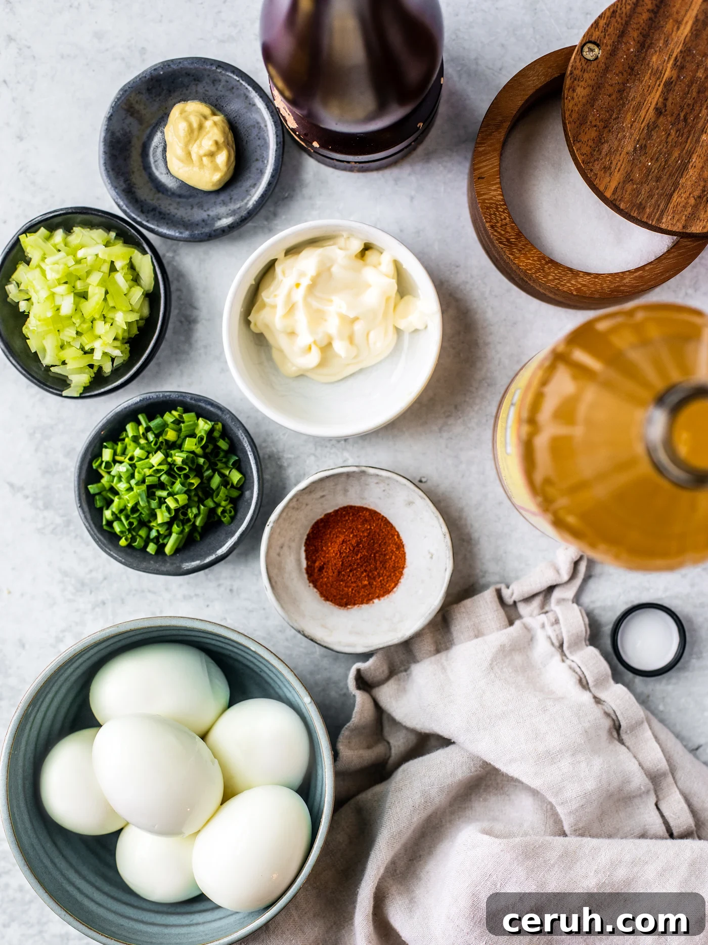 Bowl of hard-boiled eggs and pinch bowls of chives, celery, mayo. paprika, Dijon, salt, pepper, and vinegar.