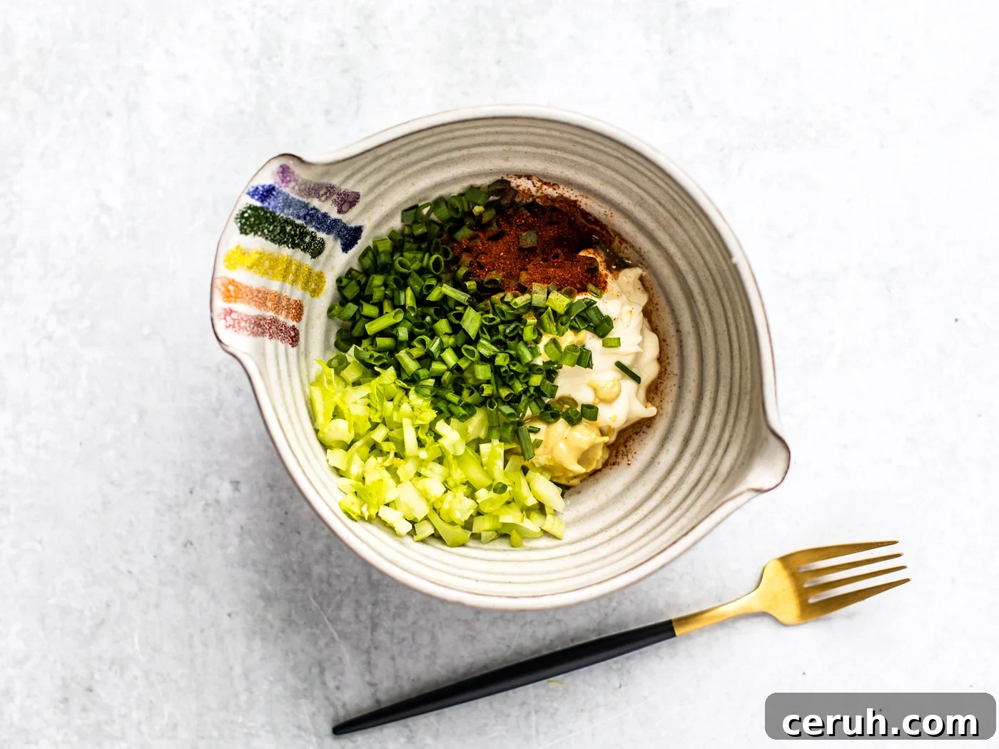 Mixing bowl full of mayo, chives, celery, and spices.