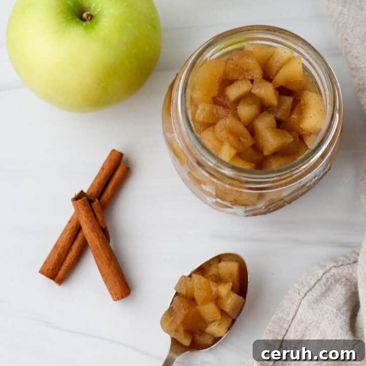 Jar of apple compote next to an apple, cinnamon sticks and a spoonful of compote.