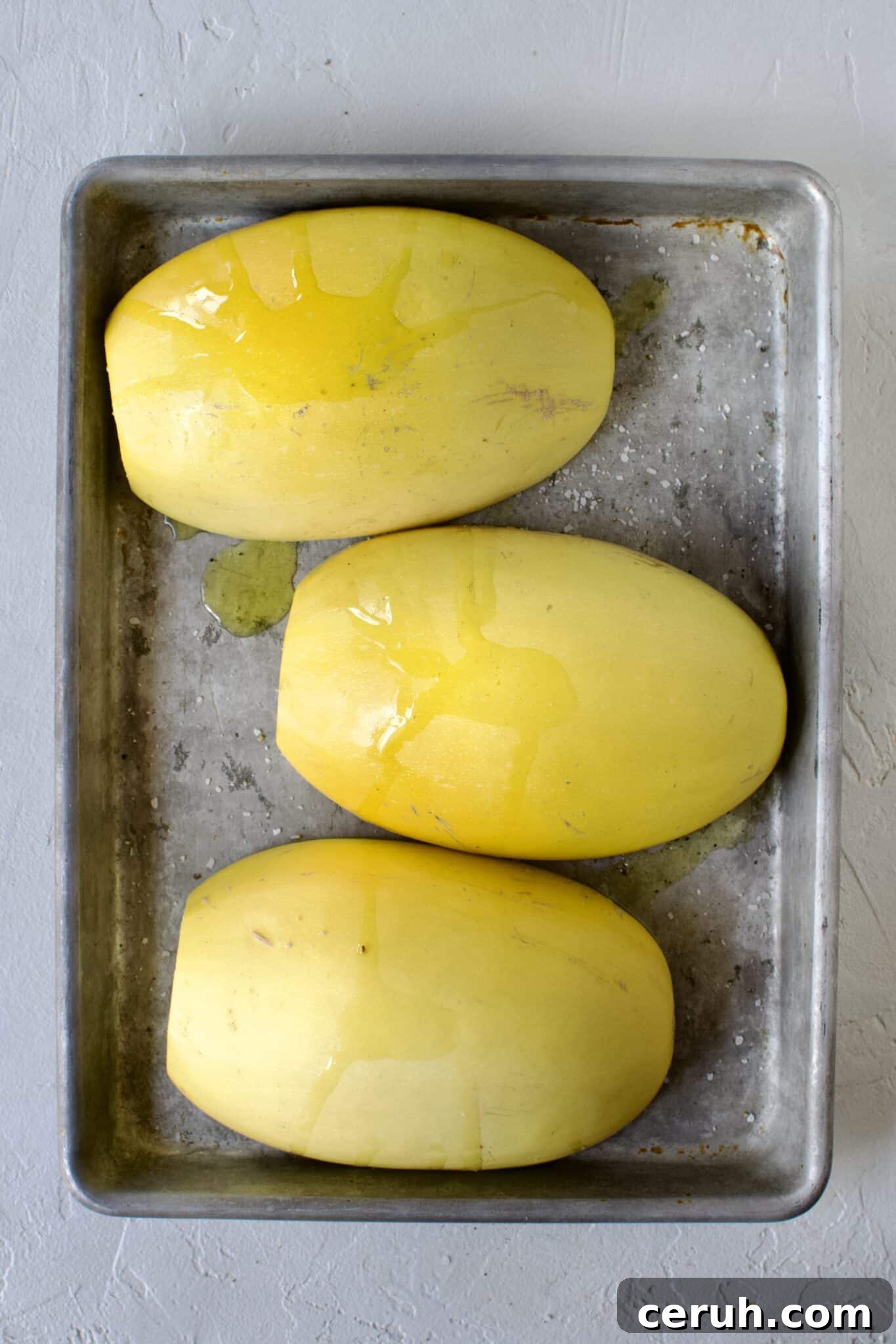 Spaghetti Squash, cut side down, seeds removed, placed on a sheet pan and seasoned with olive oil, salt, and pepper, ready to roast.