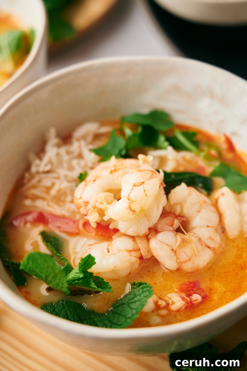 Shrimp in part of a white bowl that is filled with soup.