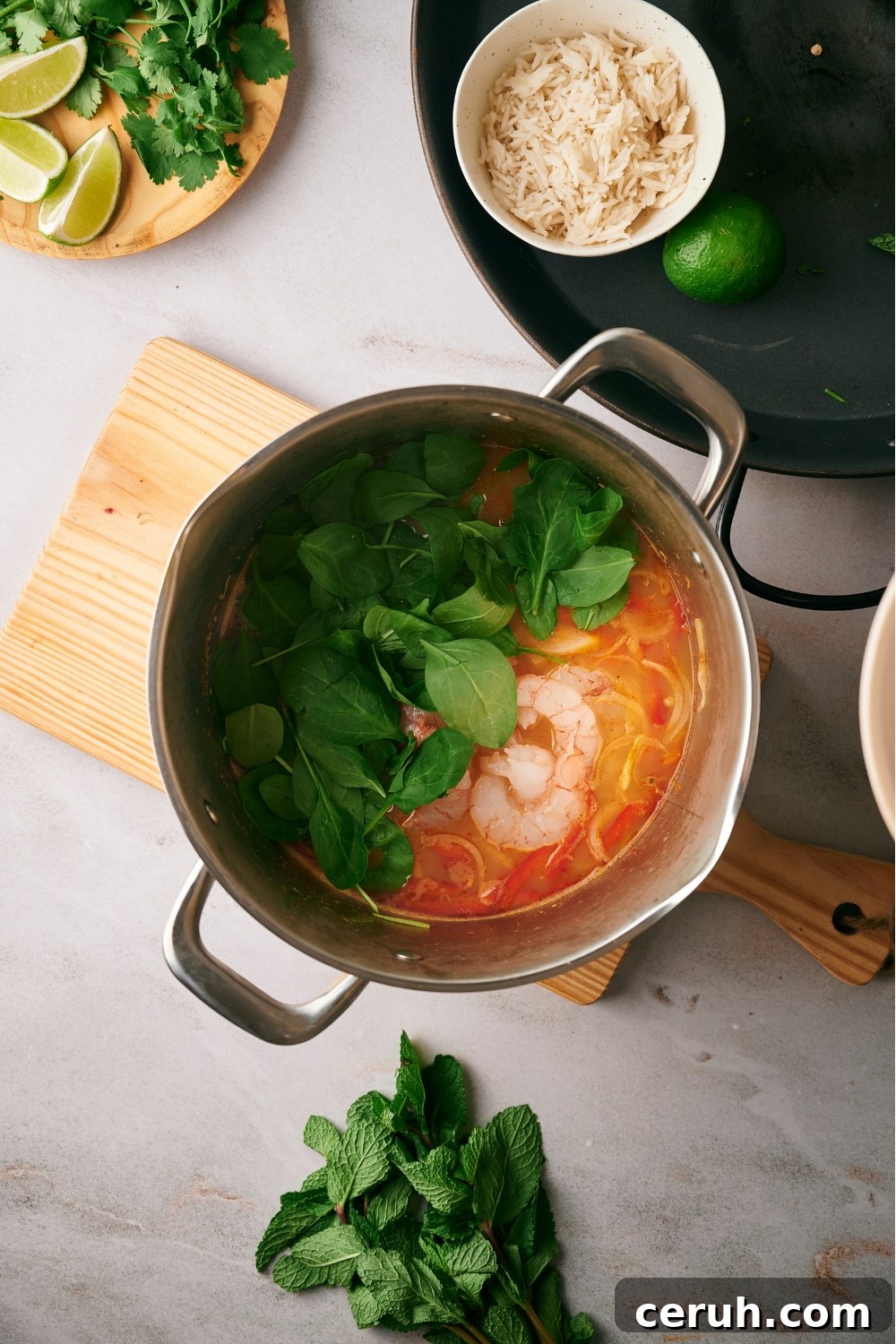 Spinach on top of shrimp in broth with sliced red bell peppers and onions.