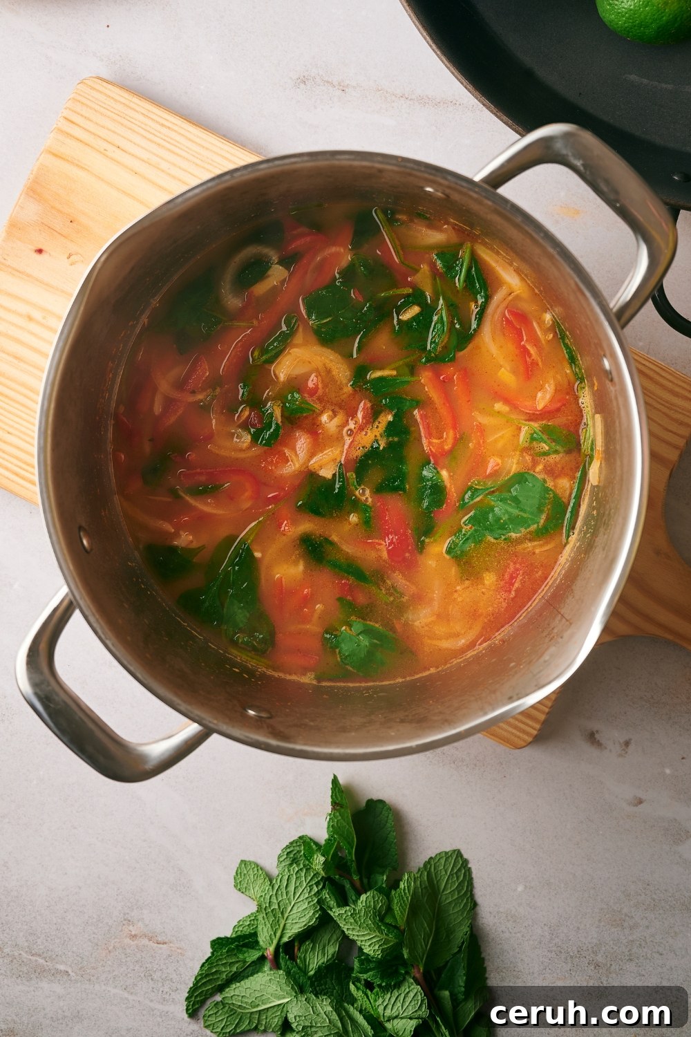 Wilted spinach, sliced red bell peppers, and onions in broth in a pot.