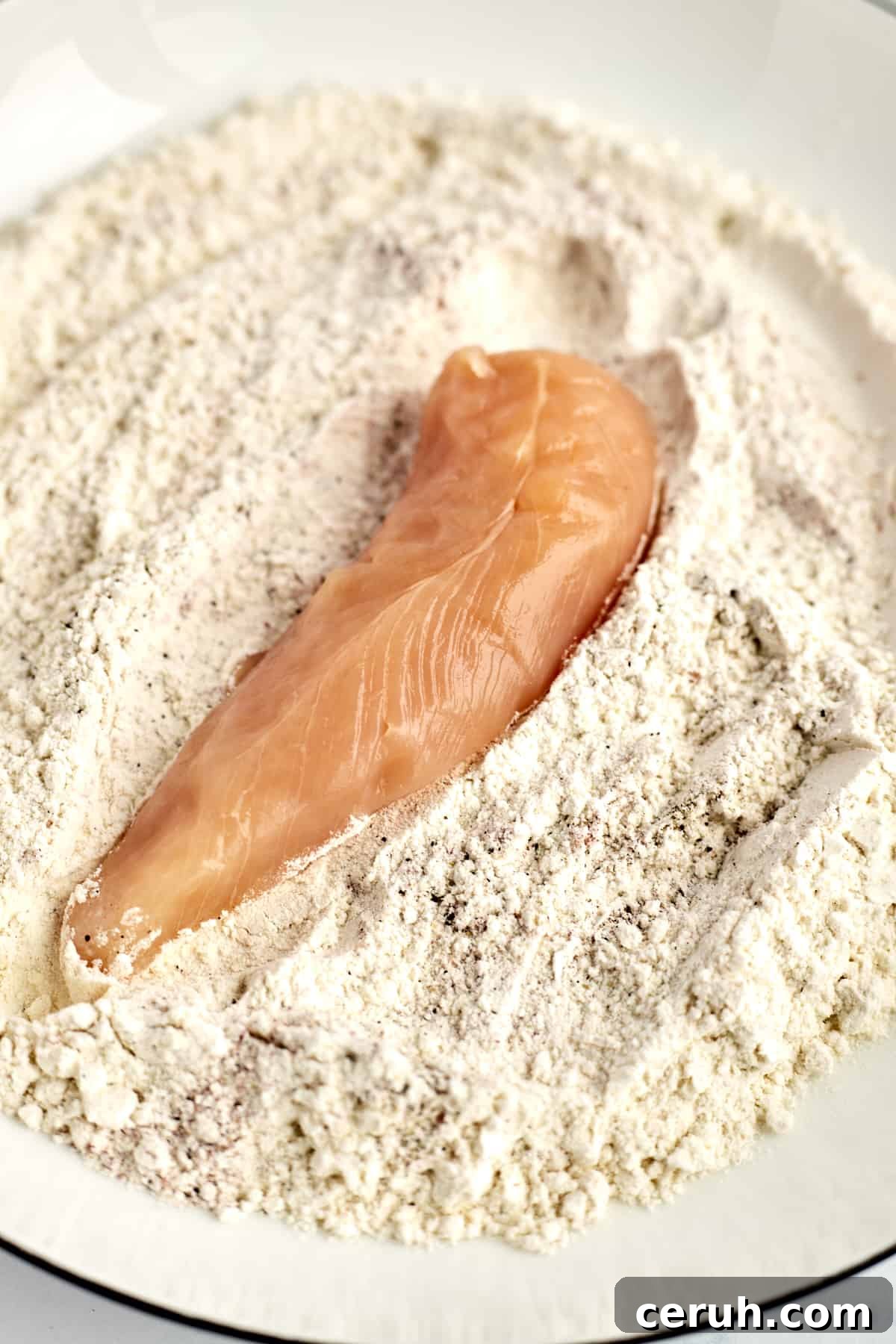 a raw chicken tender in a coconut breadcrumb mixture